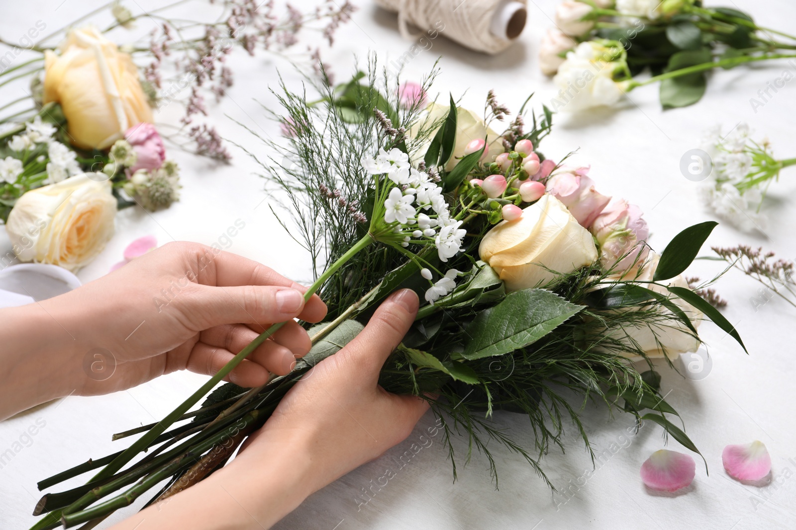 Photo of Florist making beautiful bouquet at white table, closeup