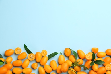Photo of Fresh ripe kumquats with green leaves on light blue background, flat lay. Space for text