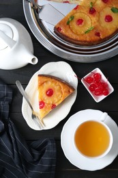 Photo of Delicious cut pineapple pie with cherry and tea served on black wooden table, flat lay