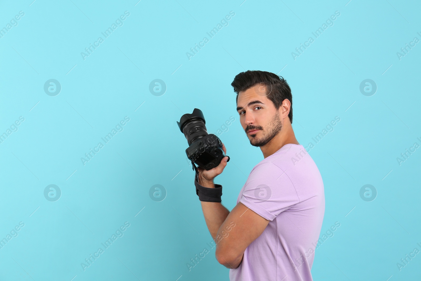 Photo of Young photographer with professional camera on light blue background. Space for text