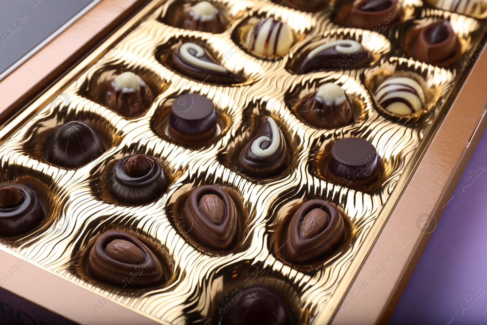 Photo of Box of delicious chocolate candies on violet background, closeup