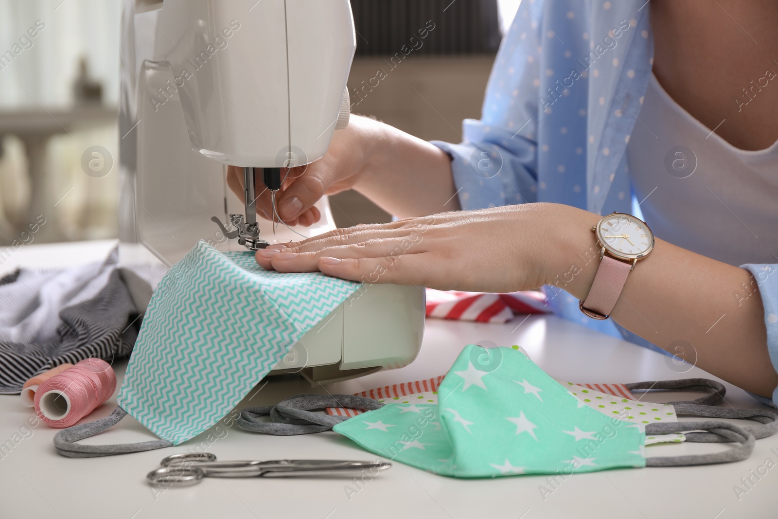 Photo of Woman making cloth mask with sewing machine at white table, closeup