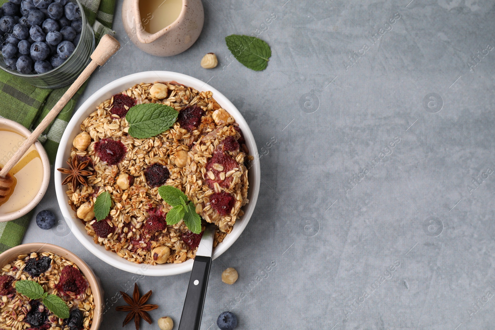 Photo of Tasty baked oatmeal with berries and nuts served on light grey table, flat lay. Space for text
