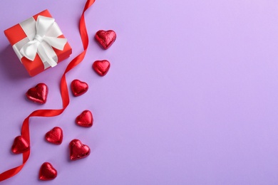 Photo of Heart shaped chocolate candies, ribbon and gift box  on violet background, flat lay. Space for text