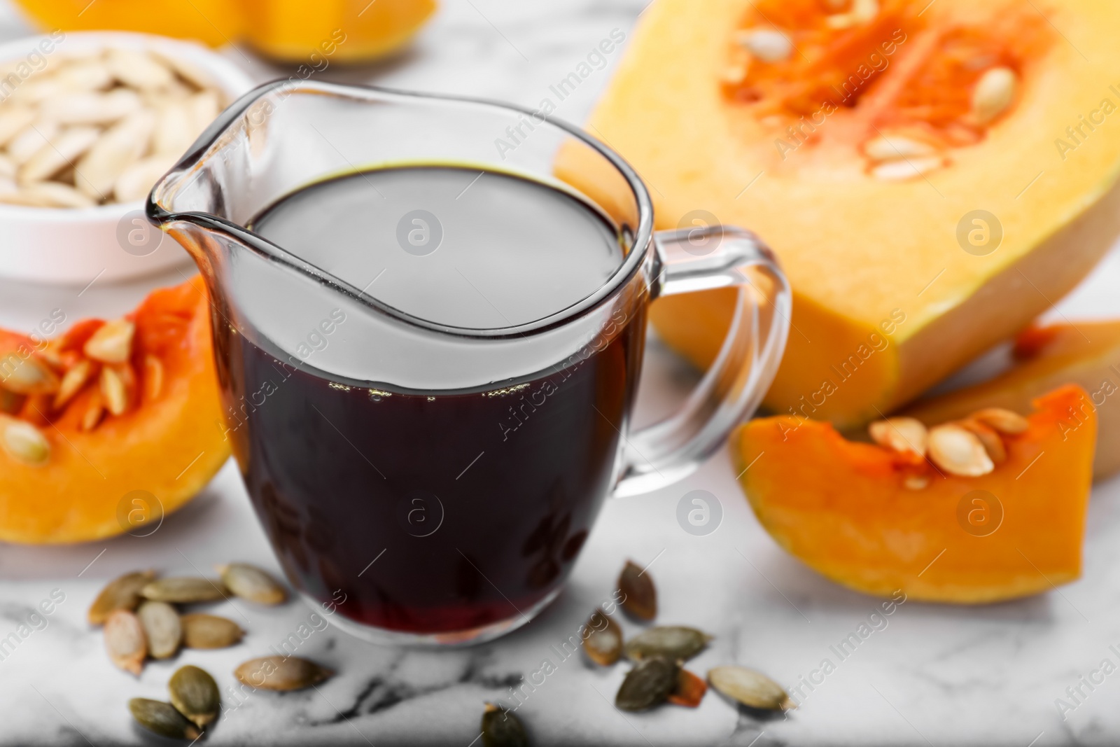 Photo of Fresh pumpkin seed oil in glass pitcher on white marble table