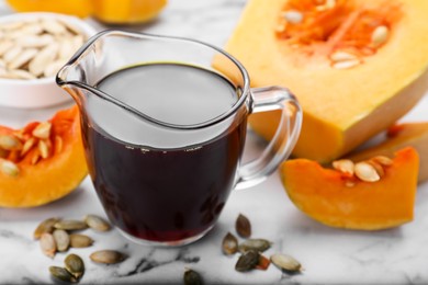 Fresh pumpkin seed oil in glass pitcher on white marble table