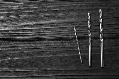 Photo of Different drill bits on black wooden table, flat lay. Space for text