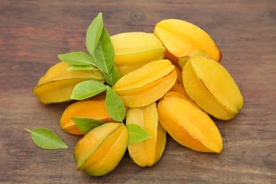 Many delicious ripe carambolas with leaves on wooden table