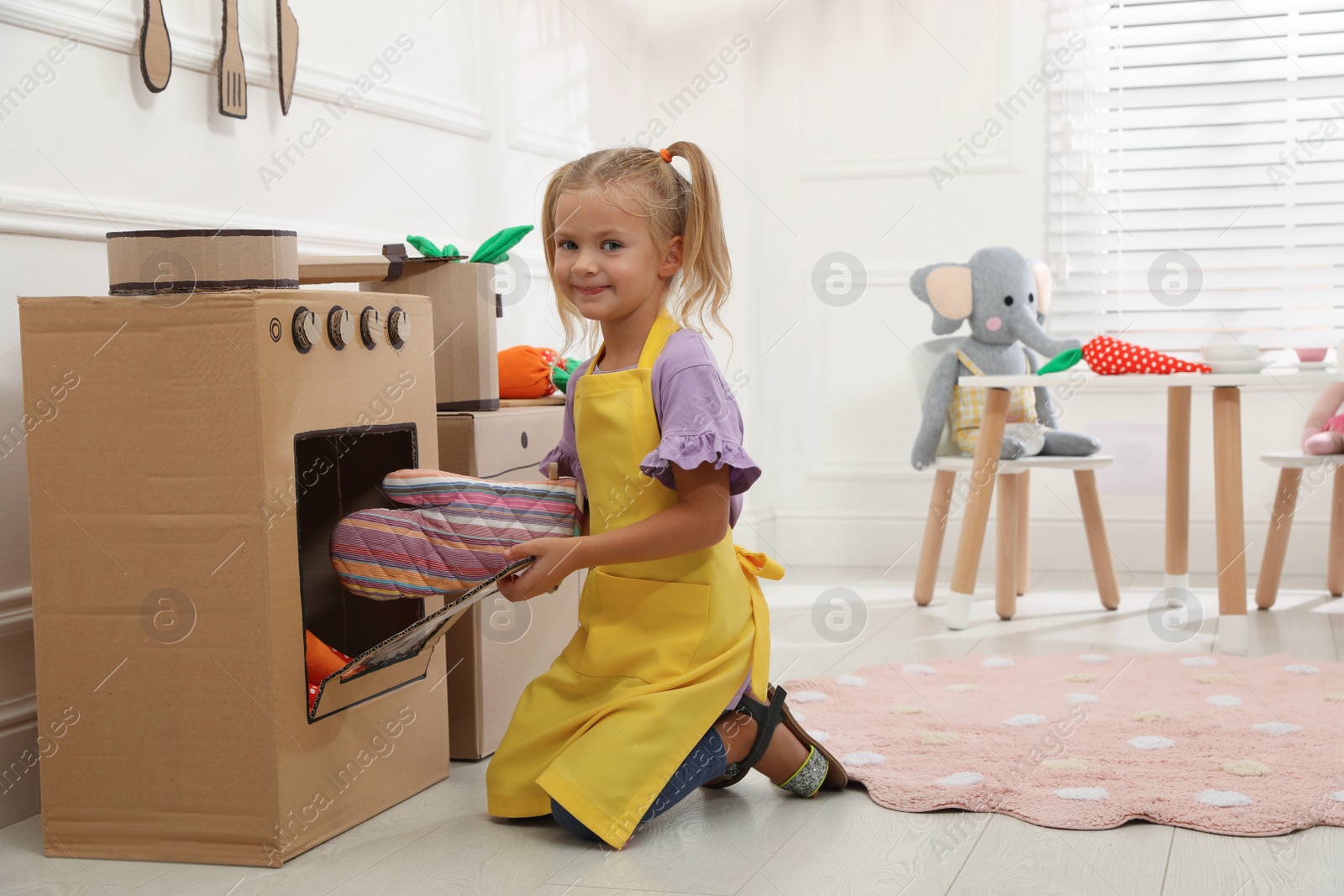 Photo of Little girl playing with toy cardboard oven at home