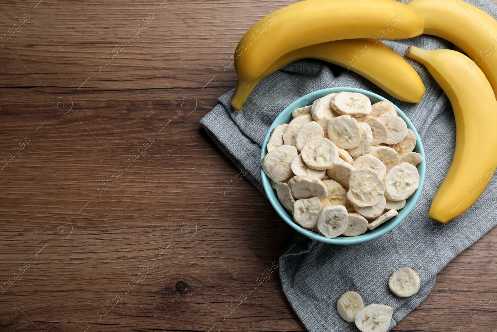 Photo of Freeze dried and fresh bananas on wooden table, top view. Space for text