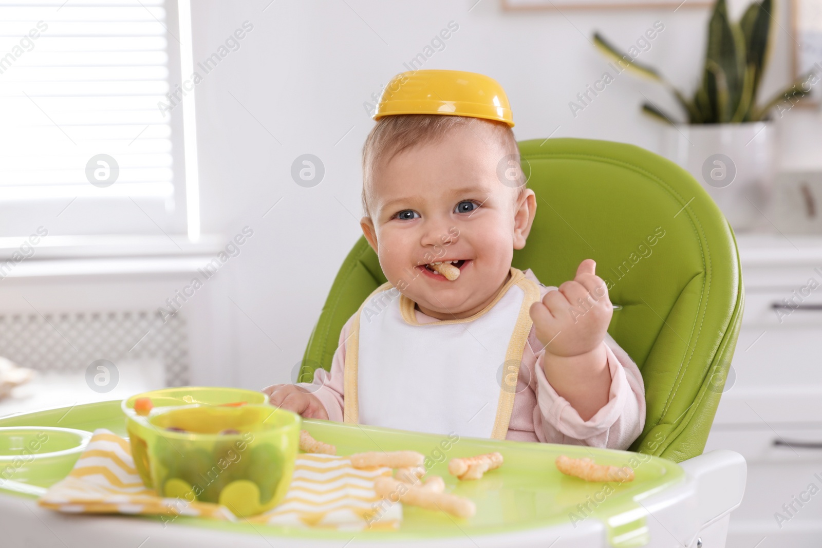 Photo of Cute little baby eating food in high chair at home