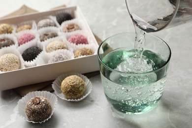Photo of Pouring water into glass and delicious vegan candy balls at light grey marble table
