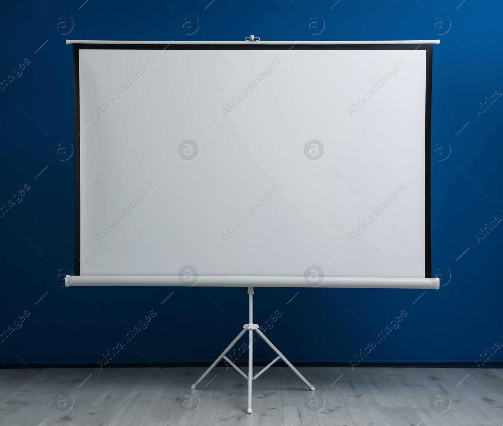 Photo of Blank projection screen near blue wall indoors. Space for design