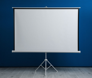 Blank projection screen near blue wall indoors. Space for design