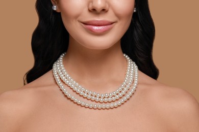 Photo of Young woman wearing elegant pearl jewelry on brown background, closeup
