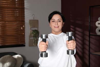 Photo of Overweight mature woman doing exercise with dumbbells at home