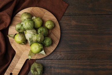 Photo of Fresh green tomatillos with husk on wooden table, top view. Space for text