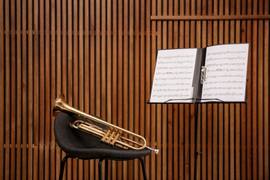 Photo of Trumpet, chair and note stand with music sheets on wooden wall background