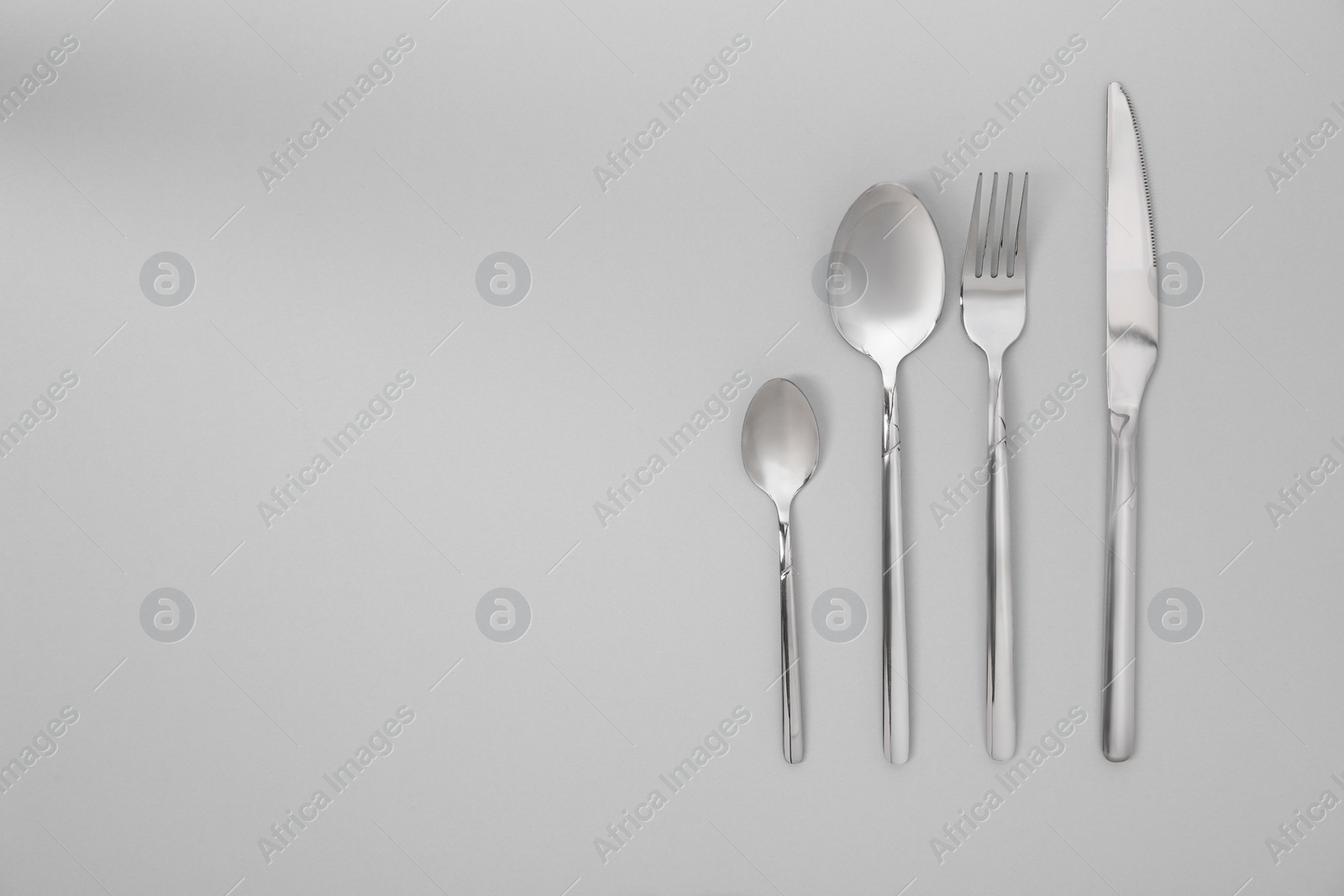 Photo of Stylish silver cutlery set on gray background, flat lay. Space for text