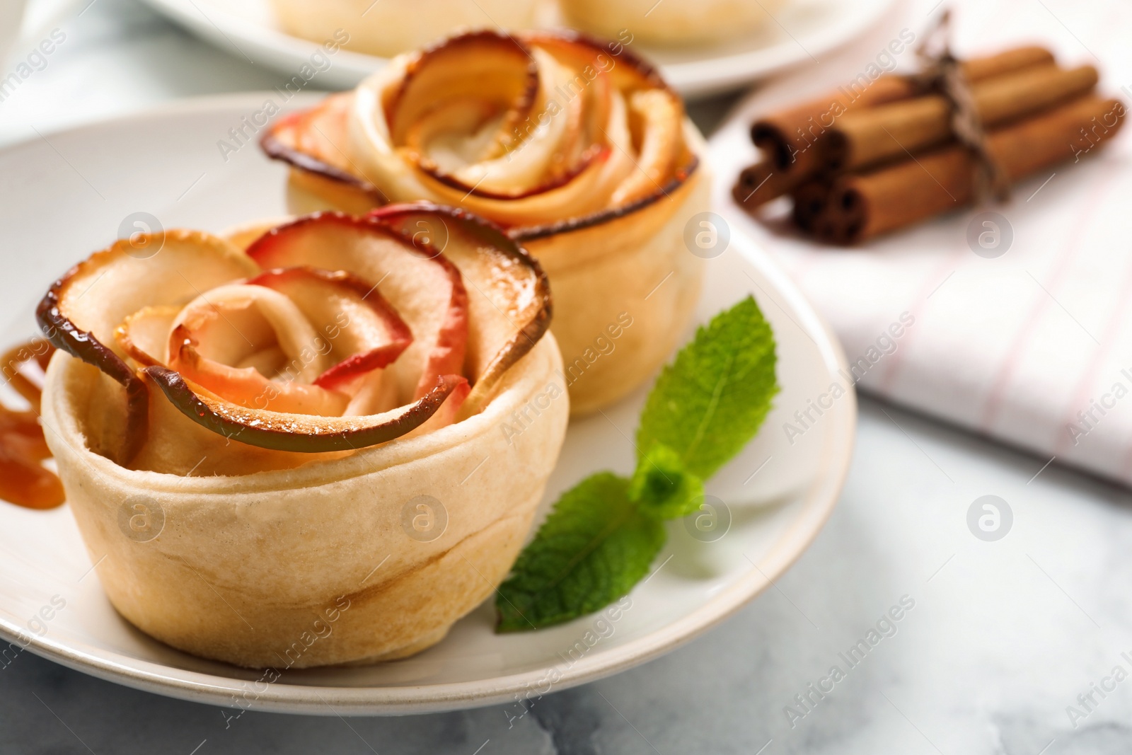 Photo of Freshly baked apple roses served on white marble table, closeup. Beautiful dessert