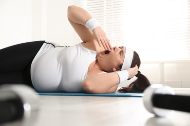 Lazy overweight woman sleeping instead of training on mat at gym