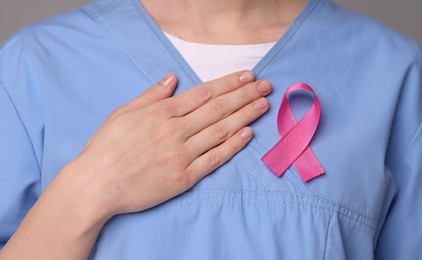 Mammologist with pink ribbon on gray background, closeup. Breast cancer awareness