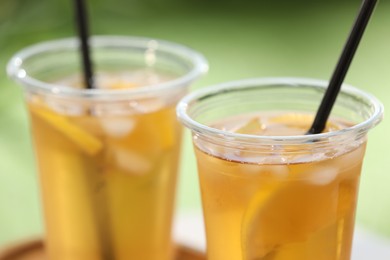 Photo of Plastic cups of tasty iced tea with lemon against blurred green background, closeup