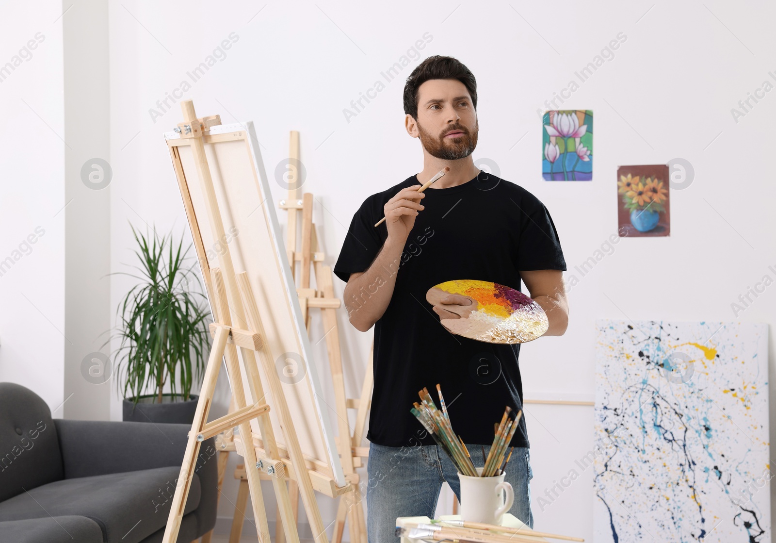 Photo of Man painting in studio. Using easel to hold canvas