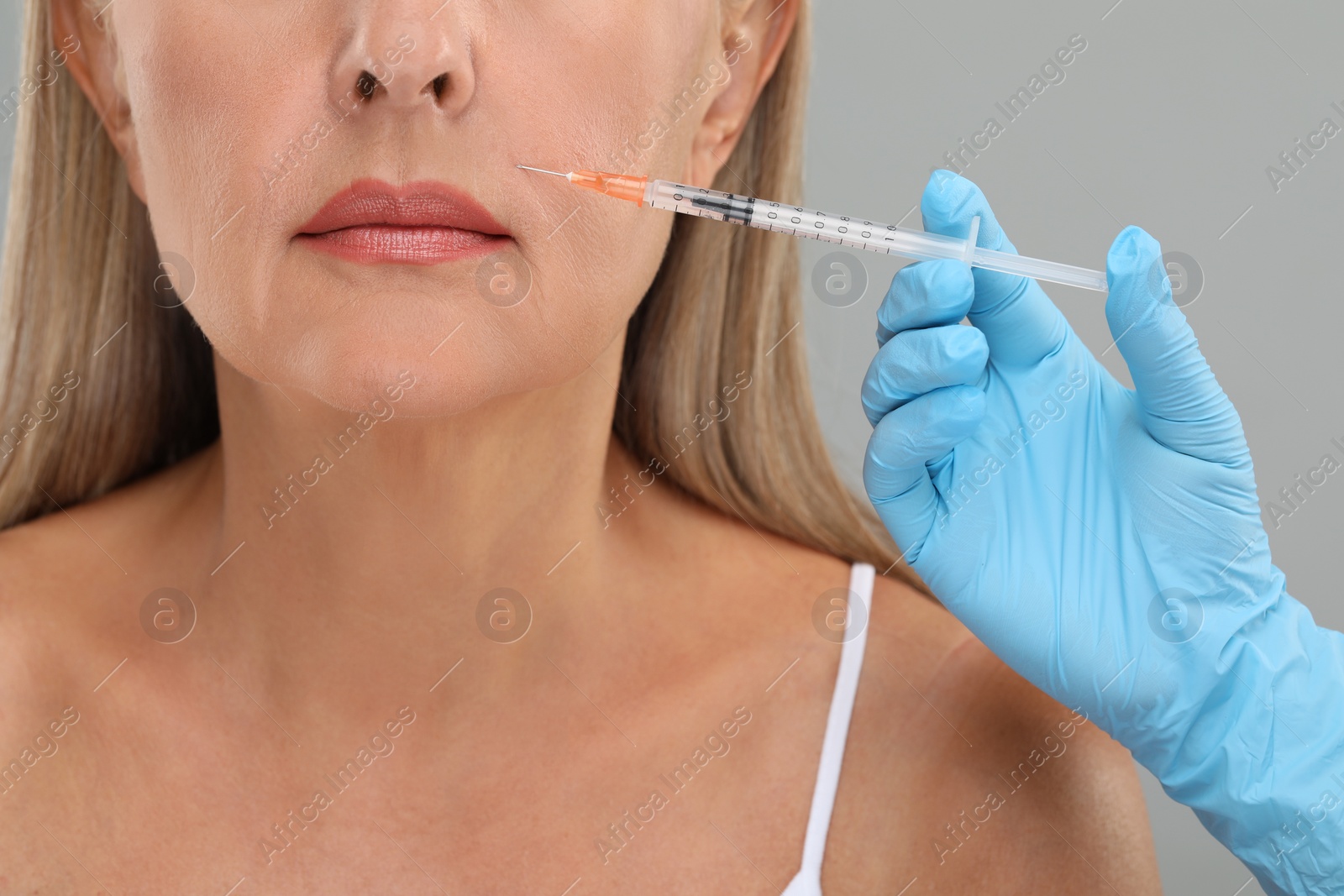 Photo of Doctor giving facial injection to senior woman on light grey background, closeup. Cosmetic surgery