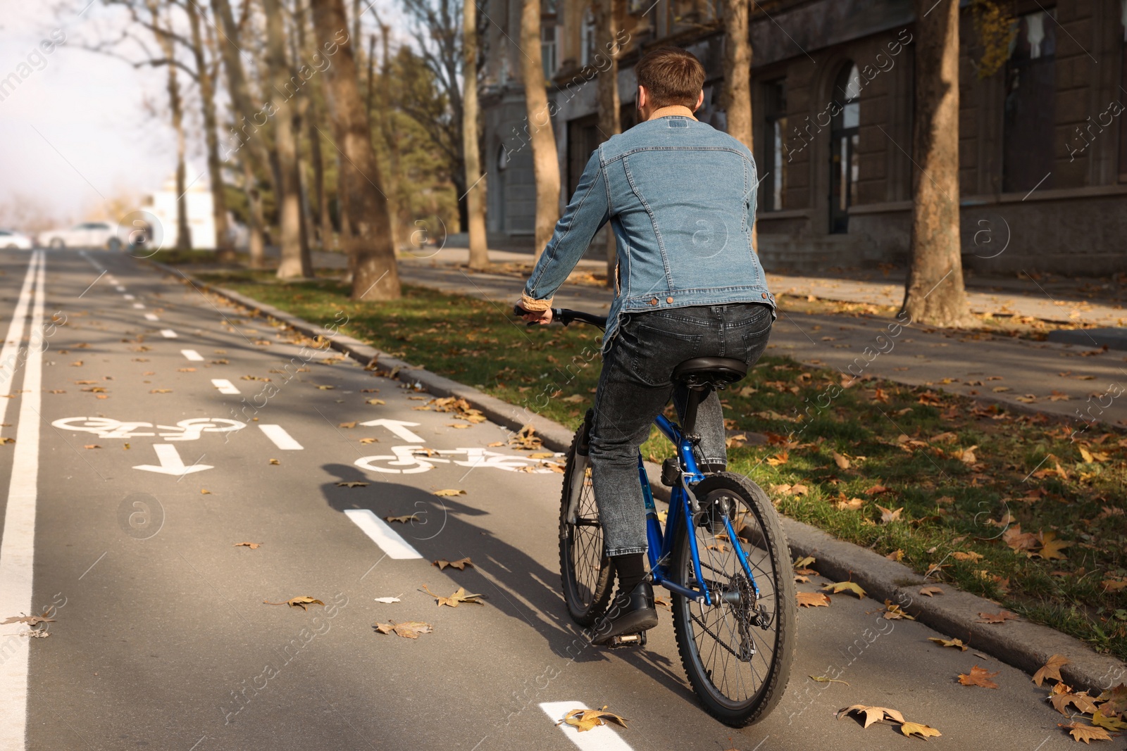 Photo of Man riding bicycle on lane in city, back view