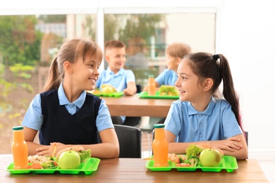Photo of Happy girls at table with healthy food in school canteen
