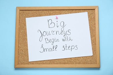 Corkboard with pinned message Big Journeys Begin With Small Steps on light blue background, top view. Motivational quote