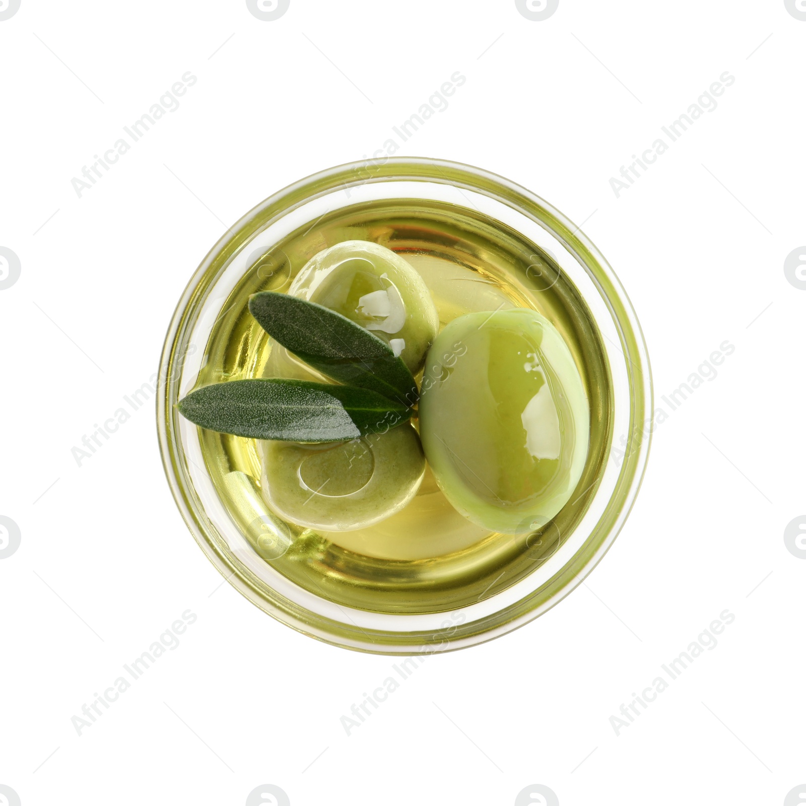 Photo of Glass bowl of oil, ripe olives and green leaves on white background, top view