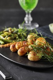 Photo of Delicious grilled potatoes with tarragon on black textured table