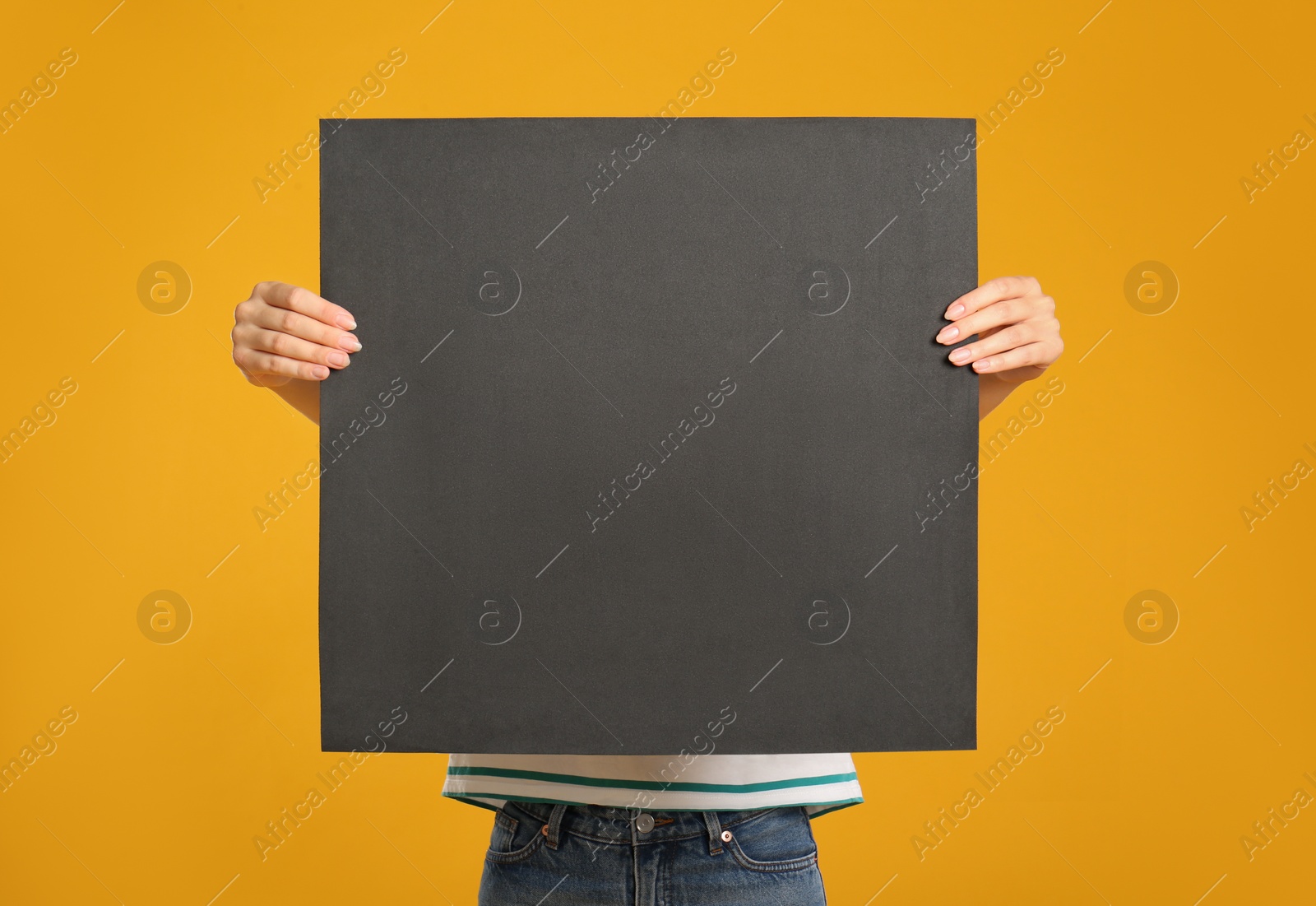 Photo of Woman holding black blank poster on yellow background. Mockup for design