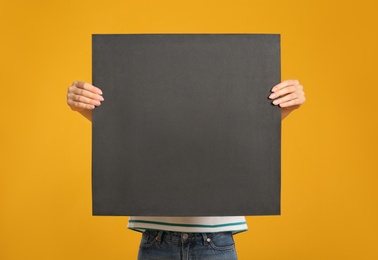 Woman holding black blank poster on yellow background. Mockup for design