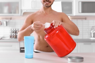 Photo of Young shirtless man preparing protein shake at table in kitchen, closeup