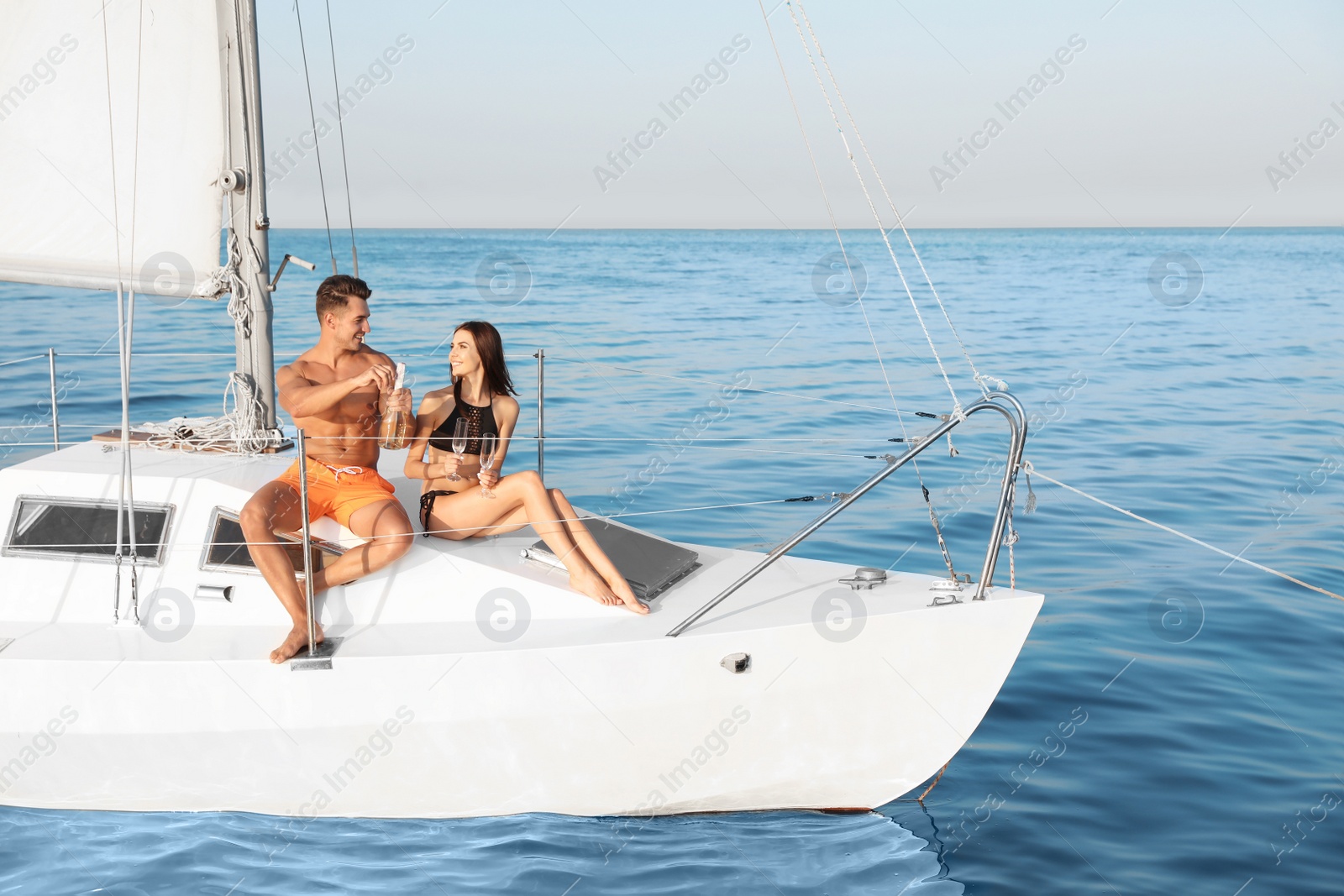 Photo of Young man and his girlfriend in bikini drinking champagne on yacht