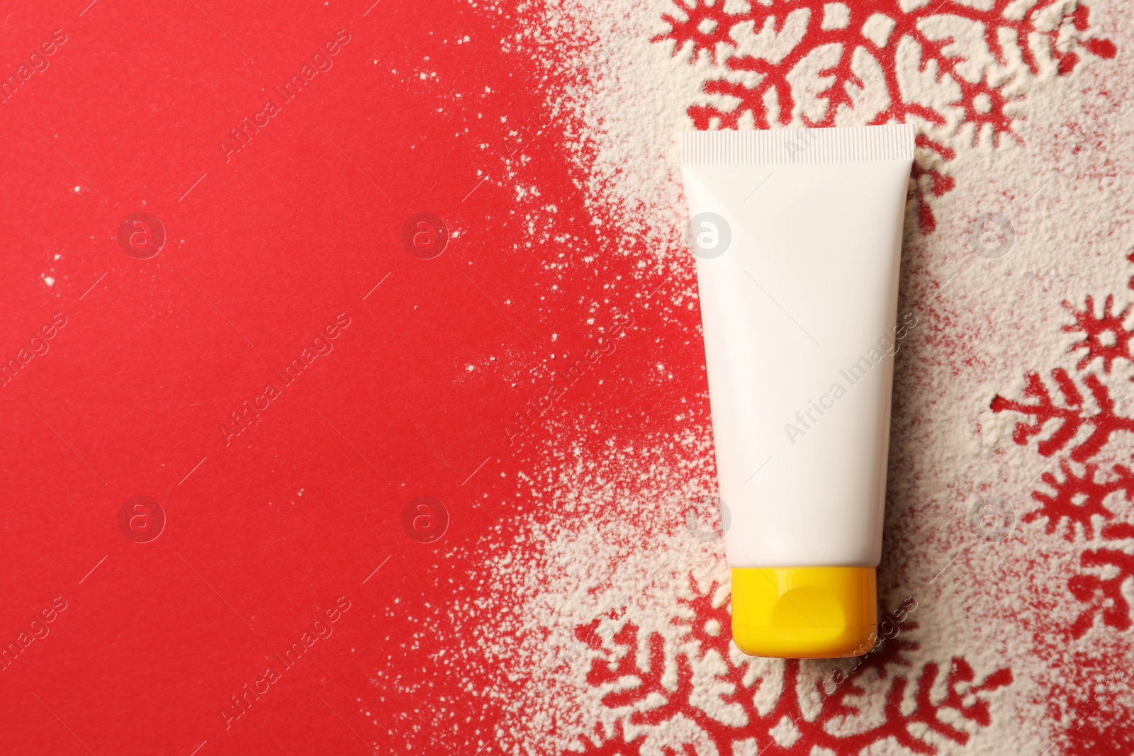 Photo of Winter skin care. Hand cream and snowflake silhouettes made with artificial snow on red background, top view. Space for text