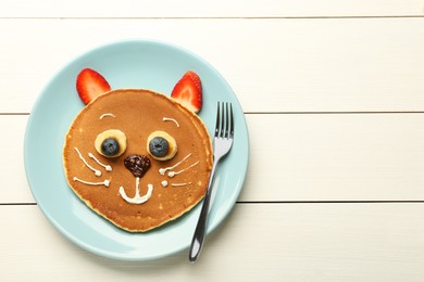 Photo of Creative serving for kids. Plate with cute cat made of pancakes, berries, cream, banana and chocolate paste on white wooden table, top view. Space for text