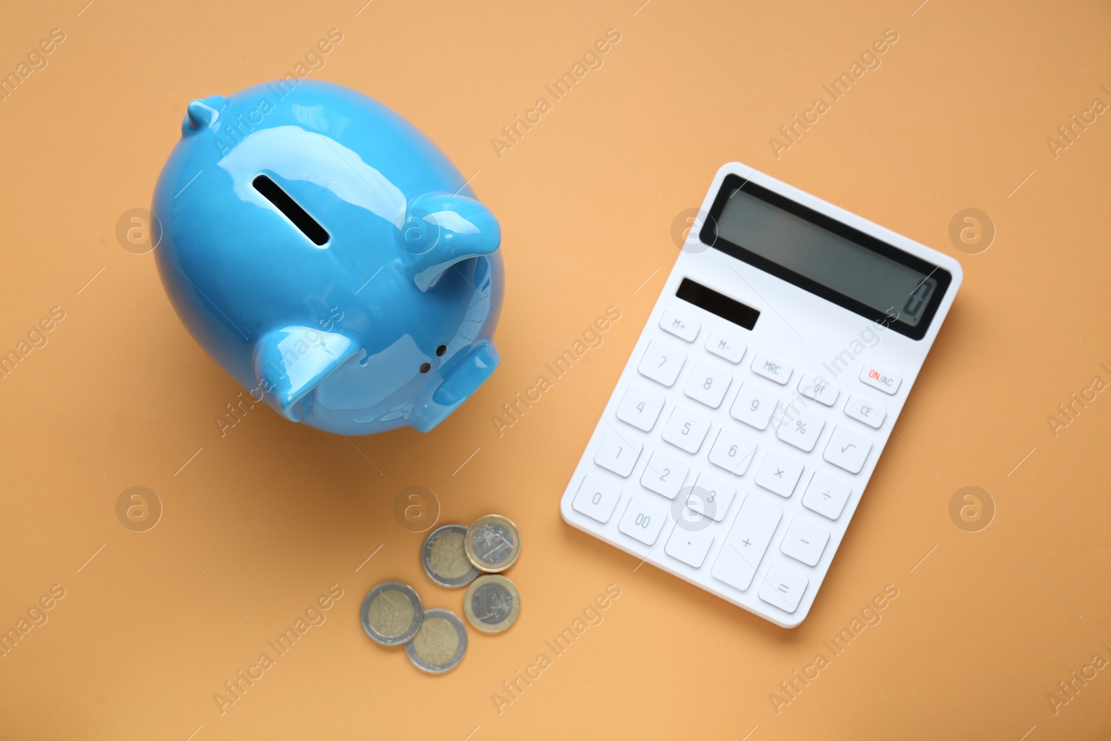 Photo of Piggy bank, coins and calculator on orange background, flat lay