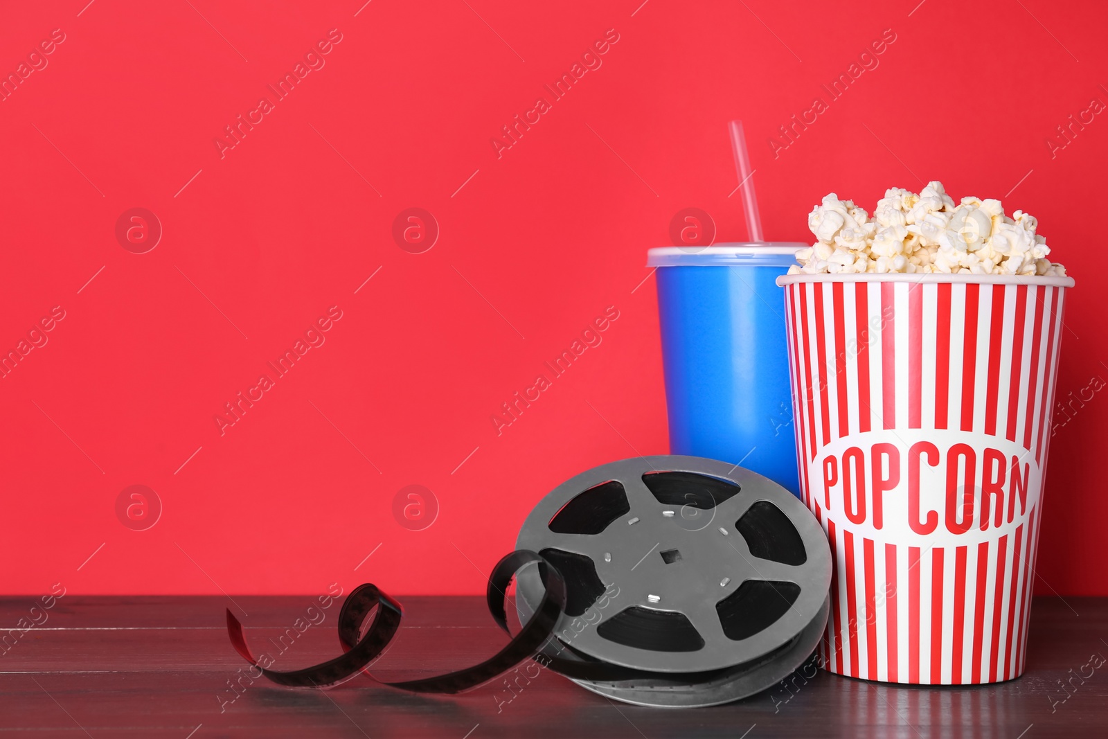 Photo of Delicious popcorn, drink and movie reel on wooden table. Space for text