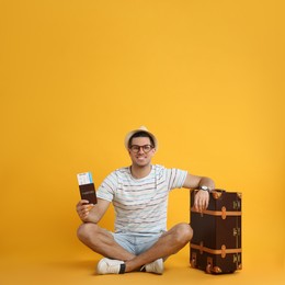 Male tourist holding passport with ticket near suitcase on yellow background