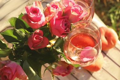 Glasses of delicious rose wine with petals, flowers and peaches on white picnic blanket outside, above view