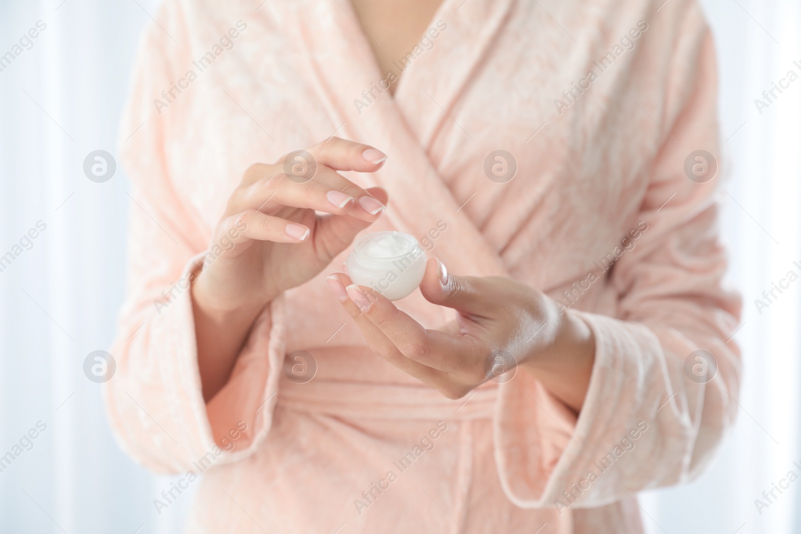 Photo of Young woman holding jar of cream at home, closeup