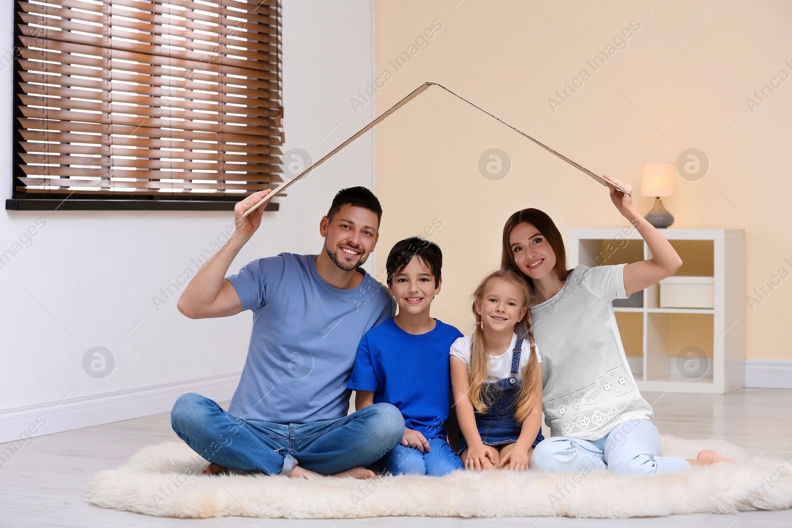 Photo of Happy family sitting under cardboard roof at home. Insurance concept