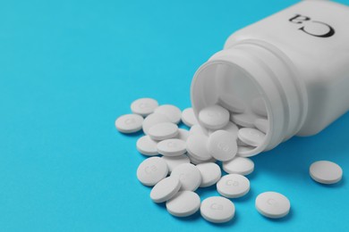 Photo of Overturned bottle of calcium supplement pills on light blue background, closeup. Space for text