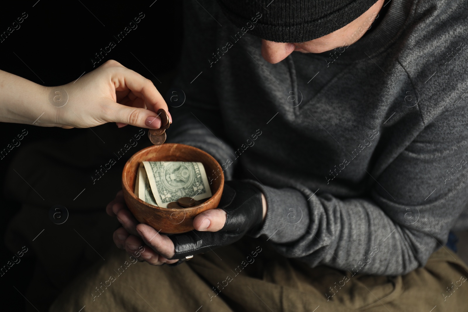 Photo of Woman giving coins to poor homeless man with bowl of donations, closeup