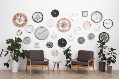 Photo of Comfortable furniture, beautiful houseplants and collection of different clocks on white wall in room