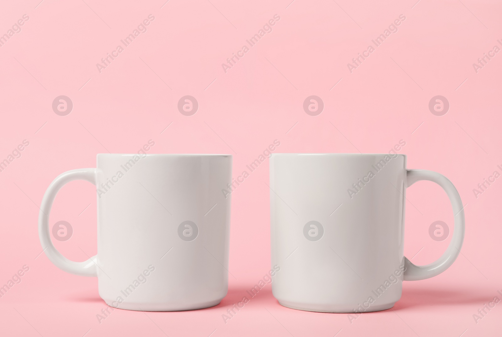 Photo of Two white ceramic mugs on pink background